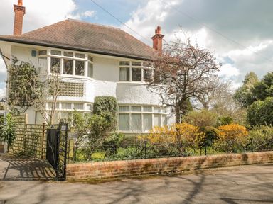 A two story house with white walls and a brown roof with garden and trees in front at West Ridge in Boscombe
