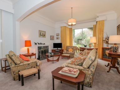 A living room with patterned armchairs, a sofa, wooden tables, a fireplace, and yellow curtains at West Ridge in Boscombe