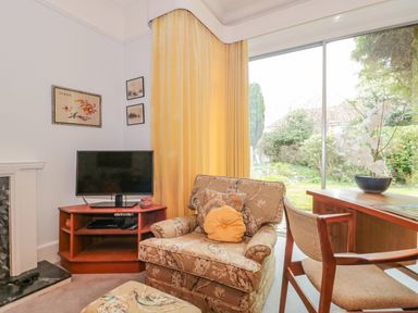 A living room with an armchair and ottoman beside a television on a wooden stand near a sliding glass door overlooking a garden at West Ridge in Boscombe
