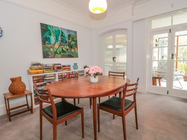 A dining room with a wooden table four chairs a bookcase with books a painting and glass doors at West Ridge in Boscombe