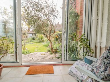 A patio door opens to a garden with plants and a tree along with a chair with cushions inside at West Ridge in Boscombe