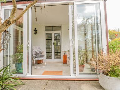 A porch area with glass sliding doors featuring two floral chairs and various potted plants at West Ridge in Boscombe