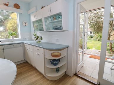 A kitchen with white cabinets a light blue countertop a dishwasher and a door leading to a garden at West Ridge in Boscombe