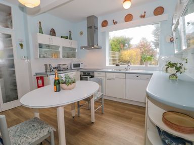 A kitchen with a white table and chairs appliances and a large window overlooking a garden at West Ridge in Boscombe
