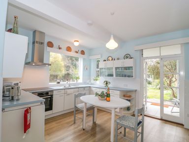 A kitchen with white cabinets a round table with two chairs and glass doors leading to a garden at West Ridge in Boscombe