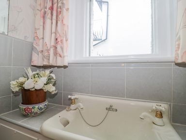 A white sink with two taps a floral curtain and a flower pot on the tiled windowsill at West Ridge in Boscombe
