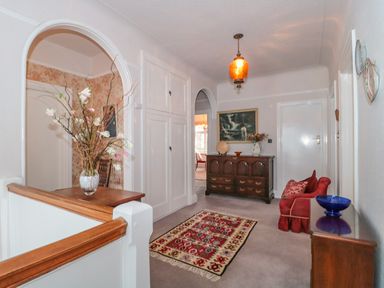 A hallway with a wooden chest of drawers a red chair a rug and a vase with flowers at West Ridge in Boscombe