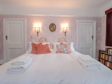 A bedroom with a double bed with pillows and towels two wall lamps a small painting two white doors and a bookshelf at West Ridge in Boscombe