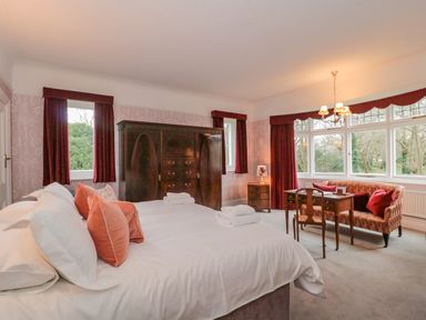 A bedroom with a large bed pillows an antique wardrobe a table with chairs and large windows at West Ridge in Boscombe