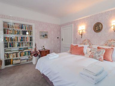 A bedroom with a double bed and floral wallpaper a bookshelf and a painting at West Ridge in Boscombe