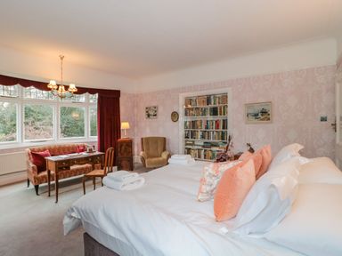 A bedroom with a large bed pillows folded towels a wooden desk chair armchair bookshelf and windows at West Ridge in Boscombe