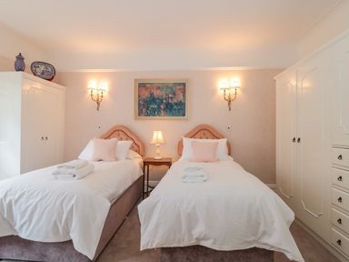A bedroom with two single beds white wardrobes and a painting on the wall at West Ridge in Boscombe