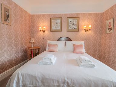 A bedroom with a bed with white linens and pink pillows bedside tables with lamps and framed pictures on the wall at West Ridge in Boscombe