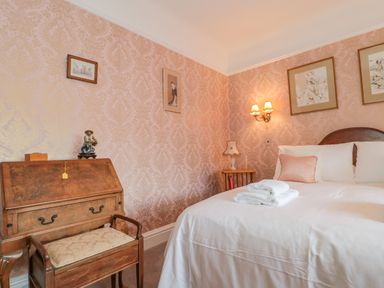 A bedroom with a bed with white linens and towels on top a wooden desk with a chair and framed pictures on the wall at West Ridge Boscombe