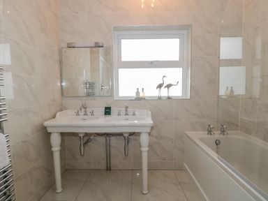A bathroom with a double sink, a mirror, a window, two bird sculptures, and a bathtub at West Ridge in Boscombe