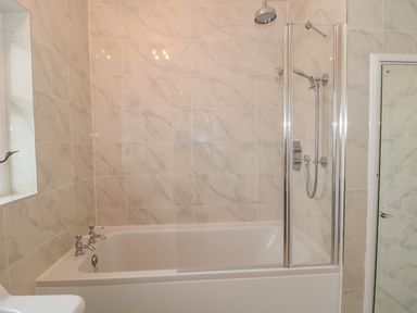 A bathroom with a white bathtub shower combination and tiled walls at West Ridge in Boscombe