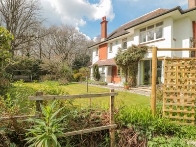 A garden with grass lawn and shrubs next to a two story house with white walls and red brick at West Ridge in Boscombe