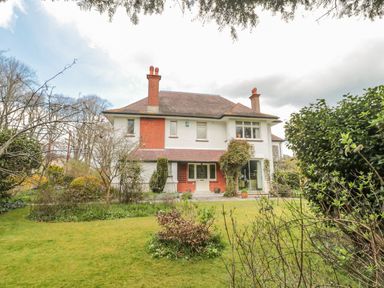 A two story house with chimneys surrounded by a garden with grass bushes and small trees at West Ridge in Boscombe