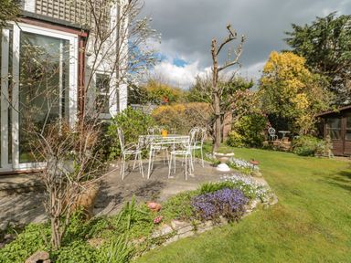 A garden with a white metal table and chairs on a patio surrounded by plants and trees at West Ridge in Boscombe