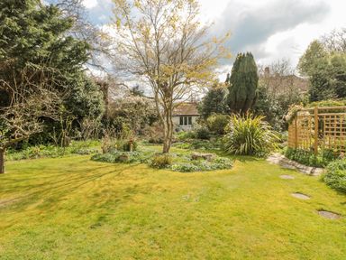 A garden with a lawn trees shrubs a stone path and a trellis with plants at West Ridge in Boscombe