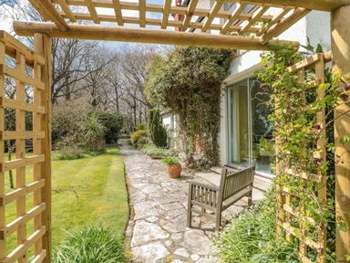 A garden pathway with a wooden bench and a wooden trellis with plants near a house at West Ridge in Boscombe