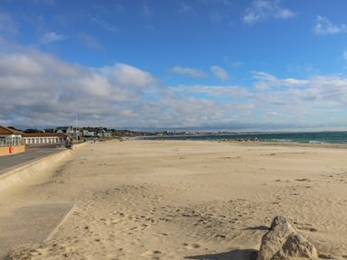 A sandy beach with a promenade and buildings on the left and ocean on the right at West Ridge in Boscombe