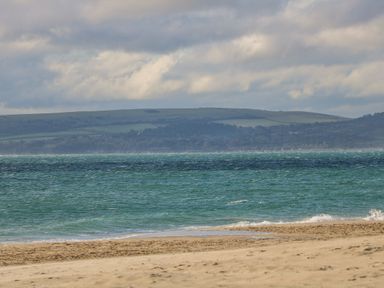 A sandy beach with waves and a green hillside in the background at West Ridge Boscombe