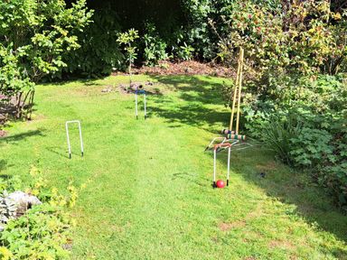 A garden with croquet equipment including hoops mallets and a ball surrounded by bushes at West Ridge in Boscombe