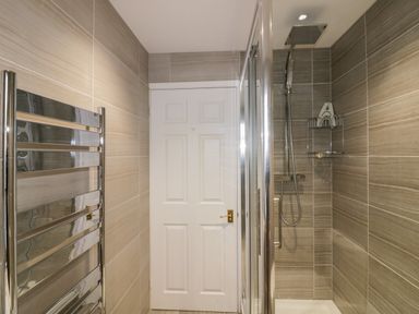 A bathroom with a shower area a glass door a white door and a chrome towel rack at Tremanners in St Agnes