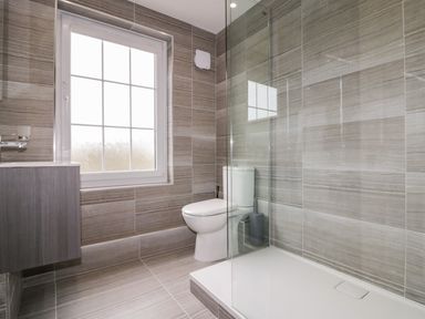 A bathroom with a toilet shower area and a sink cabinet near a window at Tremanners in St Agnes
