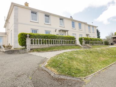 Exterior of a two-story cream-colored building with multiple windows and a hedge-lined stone balustrade in front at Tremanners in St Agnes