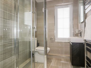 A bathroom with a glass shower enclosure a toilet a sink with a cabinet a window and a towel rail at Tremanners in St Agnes