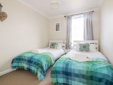 A bedroom with two single beds with green and blue checkered blankets and floral pillows at Tremanners in St Agnes