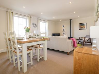 A living room and dining area with a wooden dining table set with plates and glasses and a sofa facing a wood stove at Tremanners in St Agnes