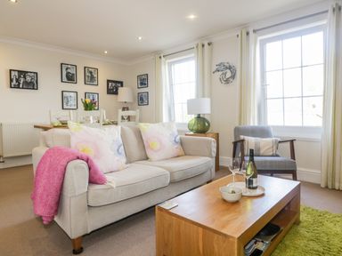 A living room with a beige sofa a pink throw a wooden coffee table and framed pictures on the wall at Tremanners in St Agnes