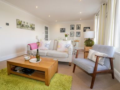 A living room with a beige sofa and wooden coffee table next to a gray armchair at Tremanners in St Agnes