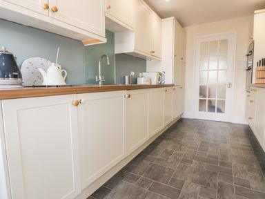 A kitchen with white cabinets wooden countertops a stainless steel faucet and a glass panel door at Tremanners in St Agnes