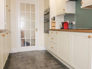 A kitchen with white cabinets a double oven a knife block a red coffee machine and a frosted glass door at Tremanners in St Agnes
