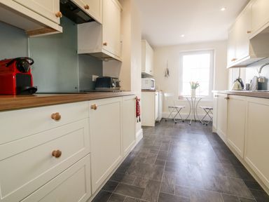 A kitchen with white cabinets a small table with two chairs and a window at Tremanners in St Agnes