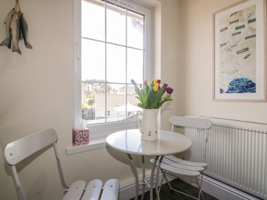 A small dining area with a round table flowers in a jug two chairs a window and a framed map on the wall at Tremanners in St Agnes