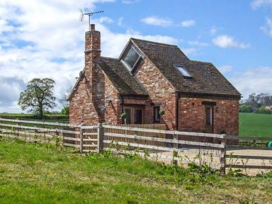 A brick house with a slate roof and a wooden fence in a grassy field at Owl Cottage in Napton-on-the-Hill near Southam