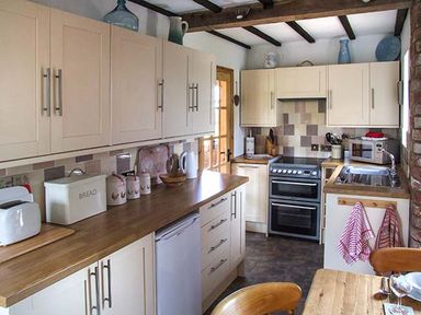 A kitchen with wooden countertops white cabinets a stove toaster and a sink at Owl Cottage in Napton-on-the-Hill near Southam