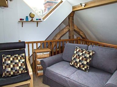 A small sitting area with a gray sofa and a black chair with checkered cushions a wooden shelf with decorative items and a skylight window at Owl Cottage in Napton-on-the-Hill near Southam