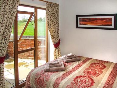 A bedroom with a bed folded towels on it a window with curtains and a view of a patio at Owl Cottage in Napton-on-the-Hill near Southam