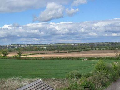 A rural landscape with green and brown fields under a partly cloudy sky at Owl Cottage in Napton-on-the-Hill near Southam