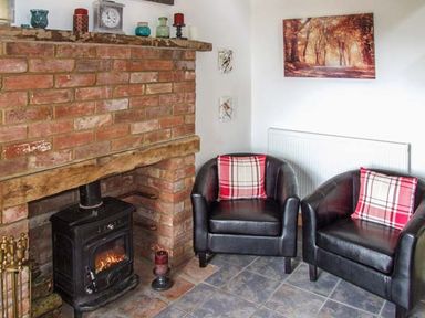 A room with a brick fireplace a black wood stove two black leather armchairs with red plaid cushions and wall decorations at Owl Cottage in Napton-on-the-Hill near Southam