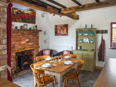 A dining room with a wooden table set for four and a brick fireplace at Owl Cottage in Napton-on-the-Hill near Southam