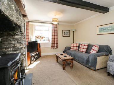 A living room with a stone fireplace a sofa with cushions a wooden coffee table and a television at Duddon Cottage in Broughton-in-Furness