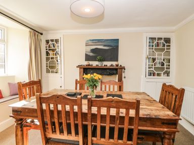 A dining room with wooden table and chairs a cabinet with books and a fireplace at Duddon Cottage in Broughton-in-Furness