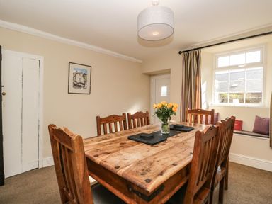 A dining room with a wooden table and six chairs with a vase of yellow flowers on the table at Duddon Cottage in Broughton-in-Furness